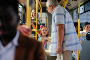 A senior man and his granddaughter are riding in the public transport